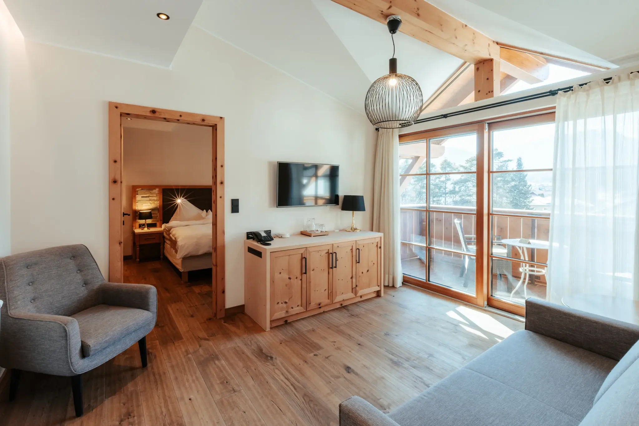 Biosuite Zirbe mit hellem Wohnraum, Zirbenholz-Sideboard, Balkon und Blick ins Schlafzimmer im Biohotel Schweitzer