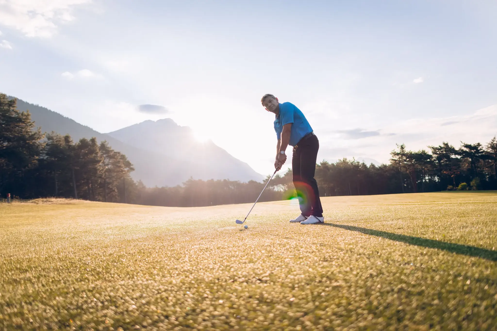 Golfer im blauen Polo schlägt im Abendlicht auf dem Golfplatz am Mieminger Sonnenplateau in Tirol ab