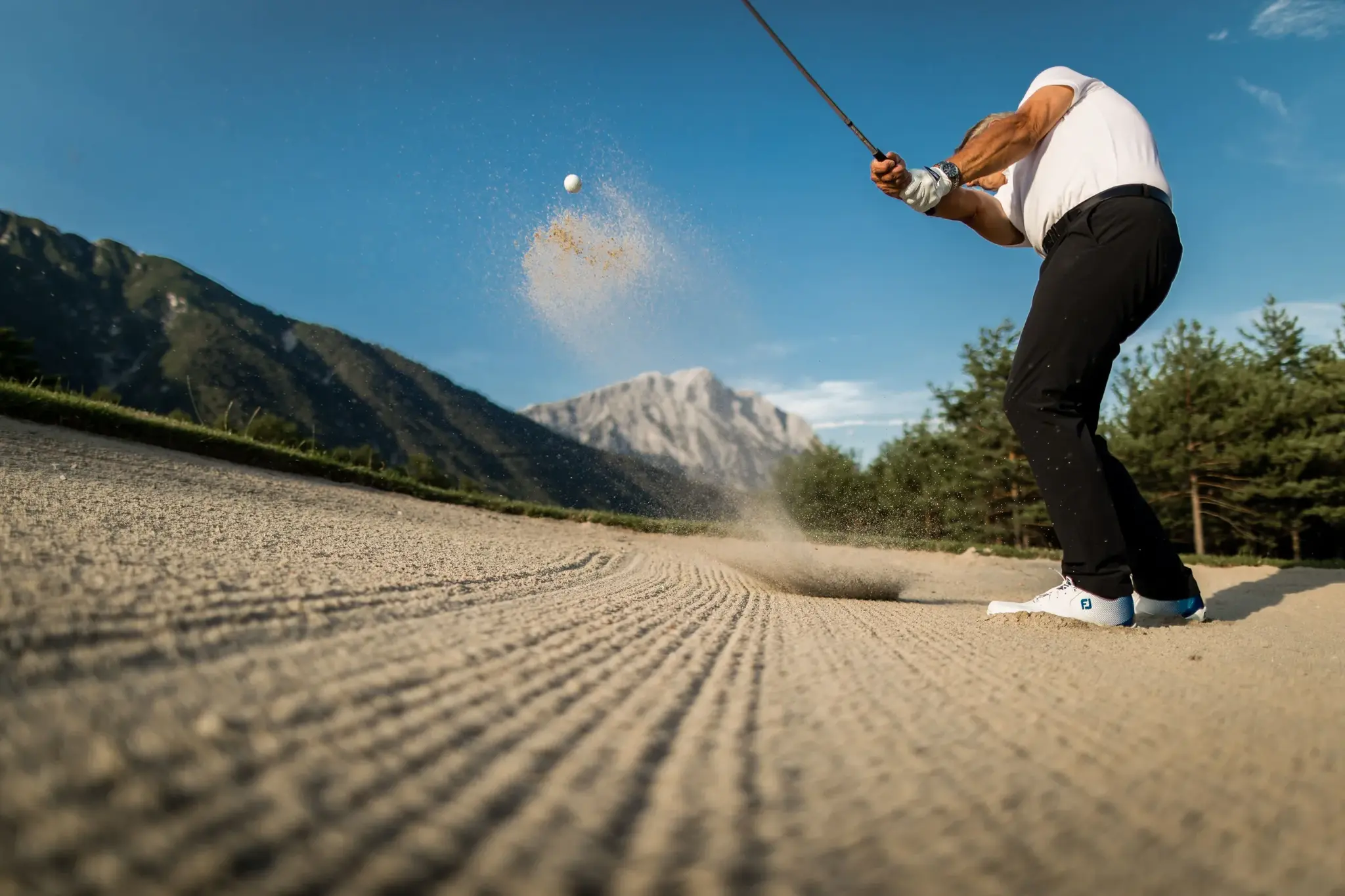 Golfer beim Bunkerschlag mit Sandfontäne auf dem Golfplatz am Mieminger Plateau vor Tiroler Bergpanorama