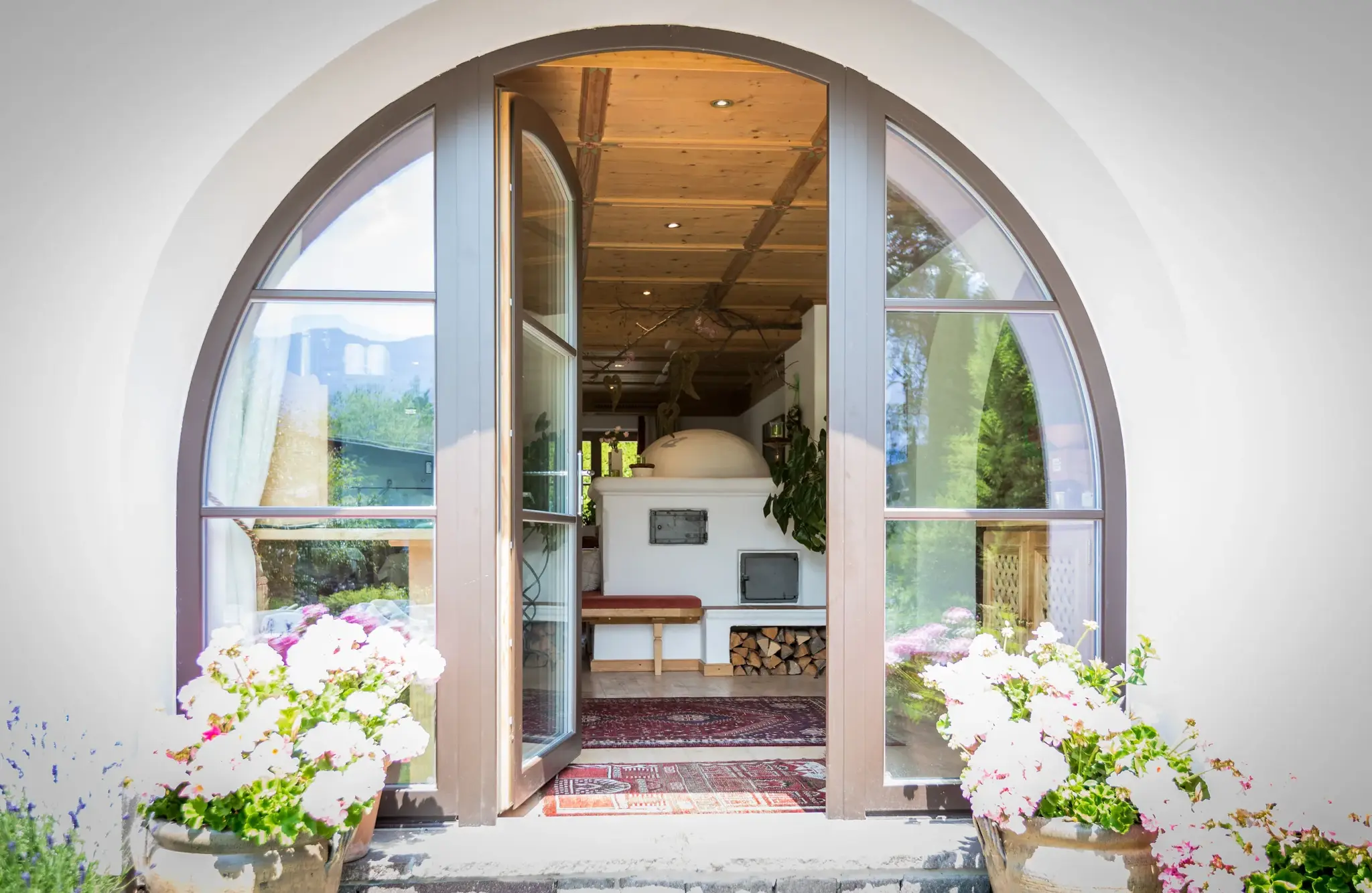 Offene Rundbogentür mit weißen Geranien gibt den Blick auf die gemütliche Kachelofen-Stube im Biohotel Schweitzer frei