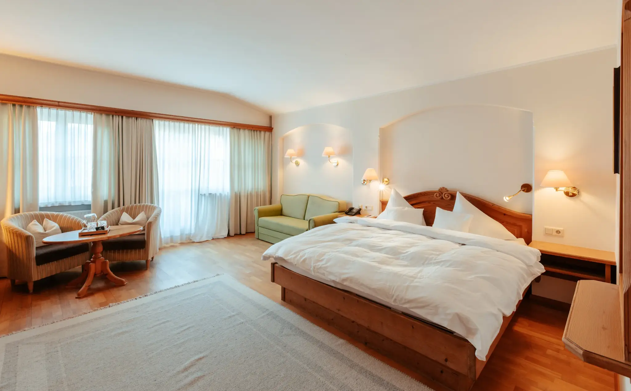 Geräumiges Wohn-Schlafzimmer im Landhausstil mit Doppelbett, Sofa und Sitzecke im Biohotel Schweitzer in Mieming