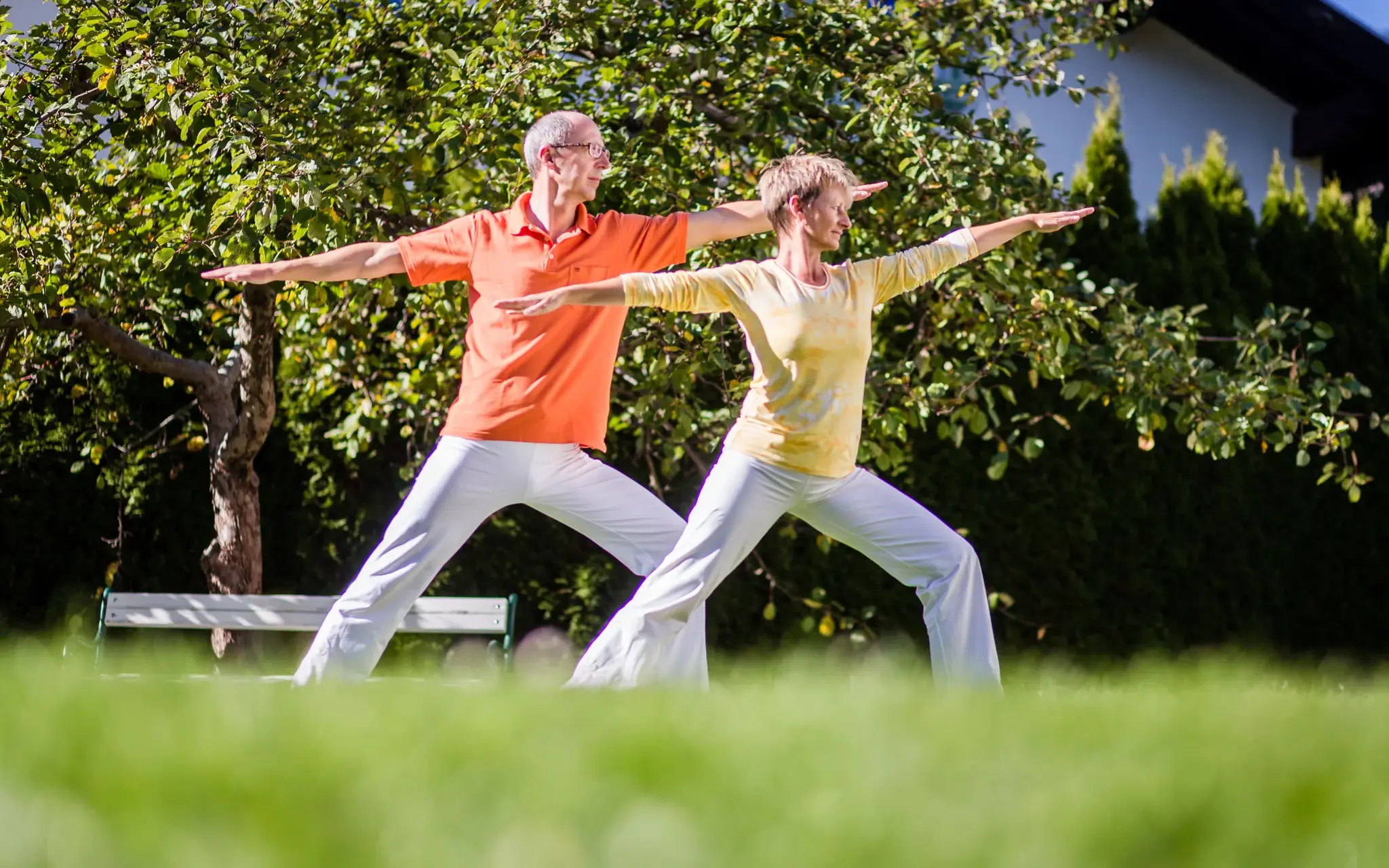 Paar in der Krieger-Pose beim Yoga-Retreat im sonnigen Garten des Biohotel Schweitzer in Tirol