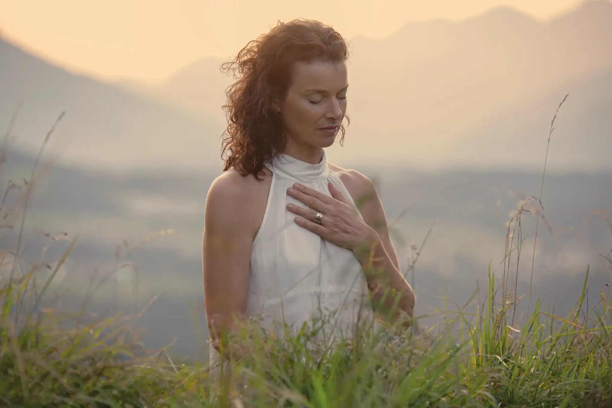 Woman with her hand on her heart and eyes closed in an alpine meadow at sunset, a moment of mindfulness during the fasting week in Tyrol
