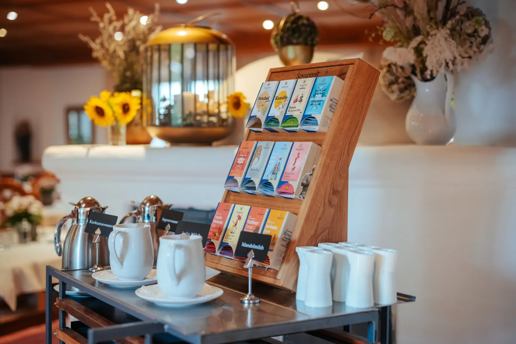 Breakfast station with organic herbal teas and small white porcelain pots, sunflowers and dried flowers at Biohotel Schweitzer