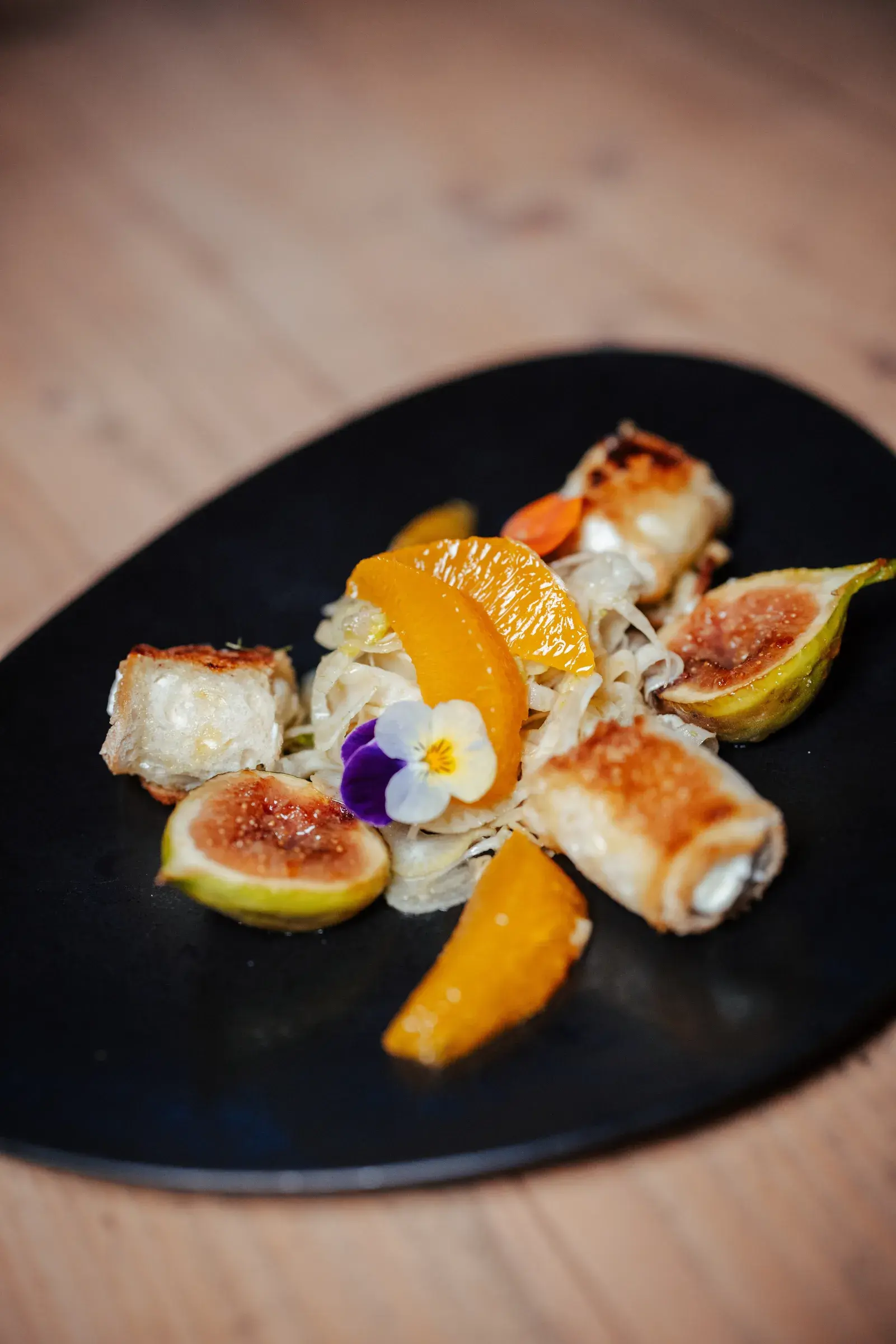 Baked goat's cheese rolls with figs, oranges and fennel on a black plate, organic cuisine at Restaurant Greenvieh