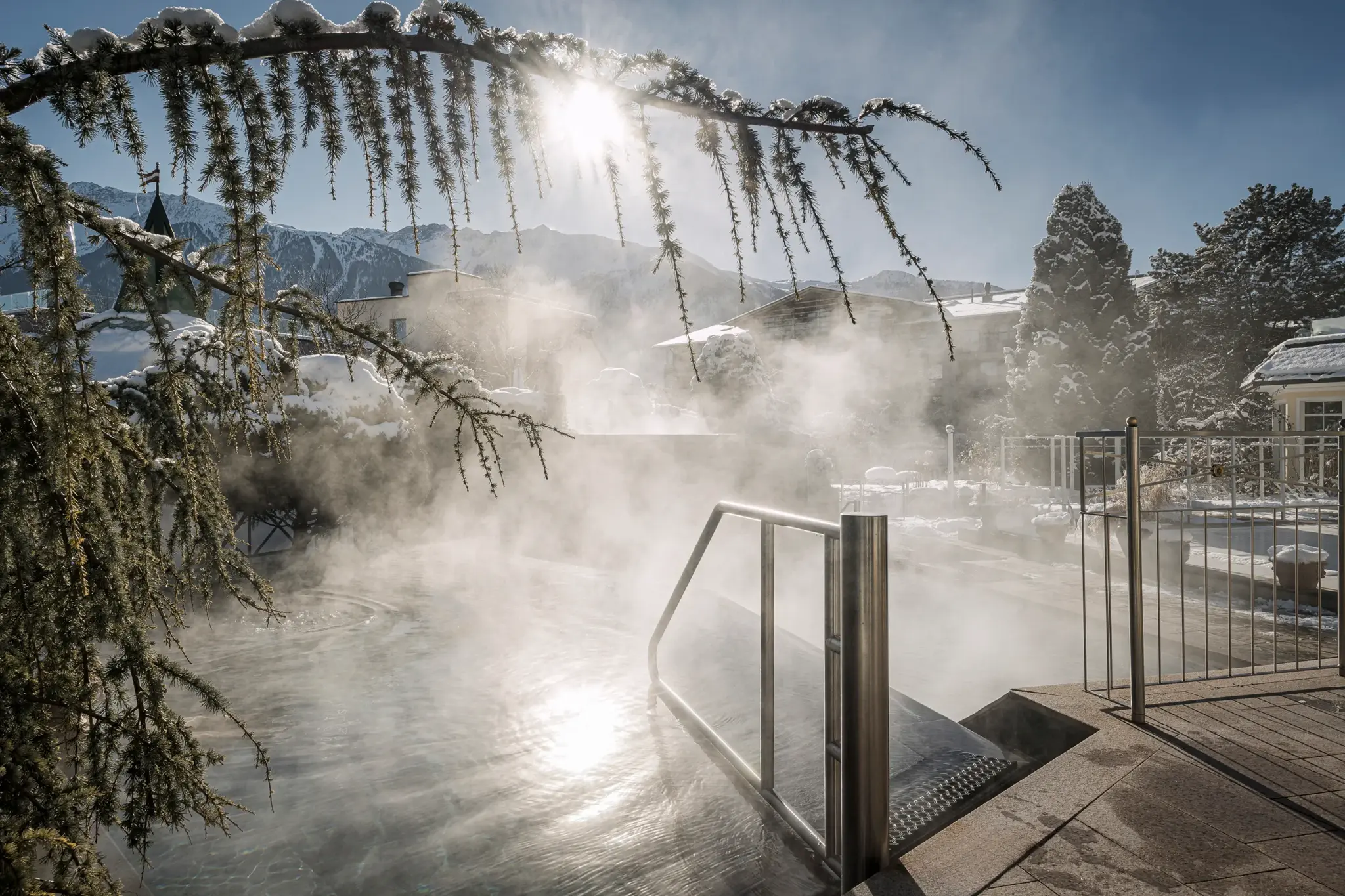 Steaming heated outdoor pool in winter snow with sunshine and a mountain panorama at Alpenresort Schwarz