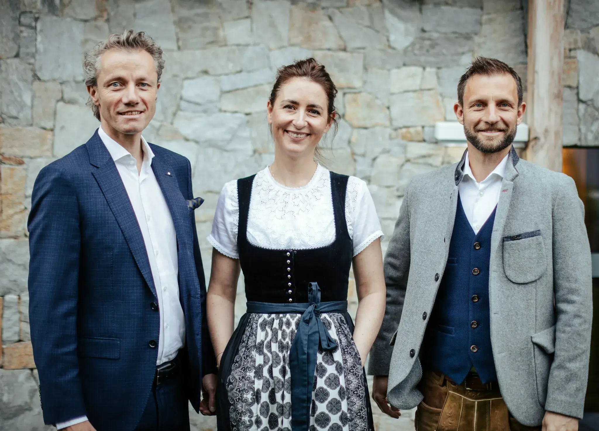 Gastgeberfamilie Pirktl in Tiroler Tracht vor der Natursteinwand des Biohotel Schweitzer in Mieming