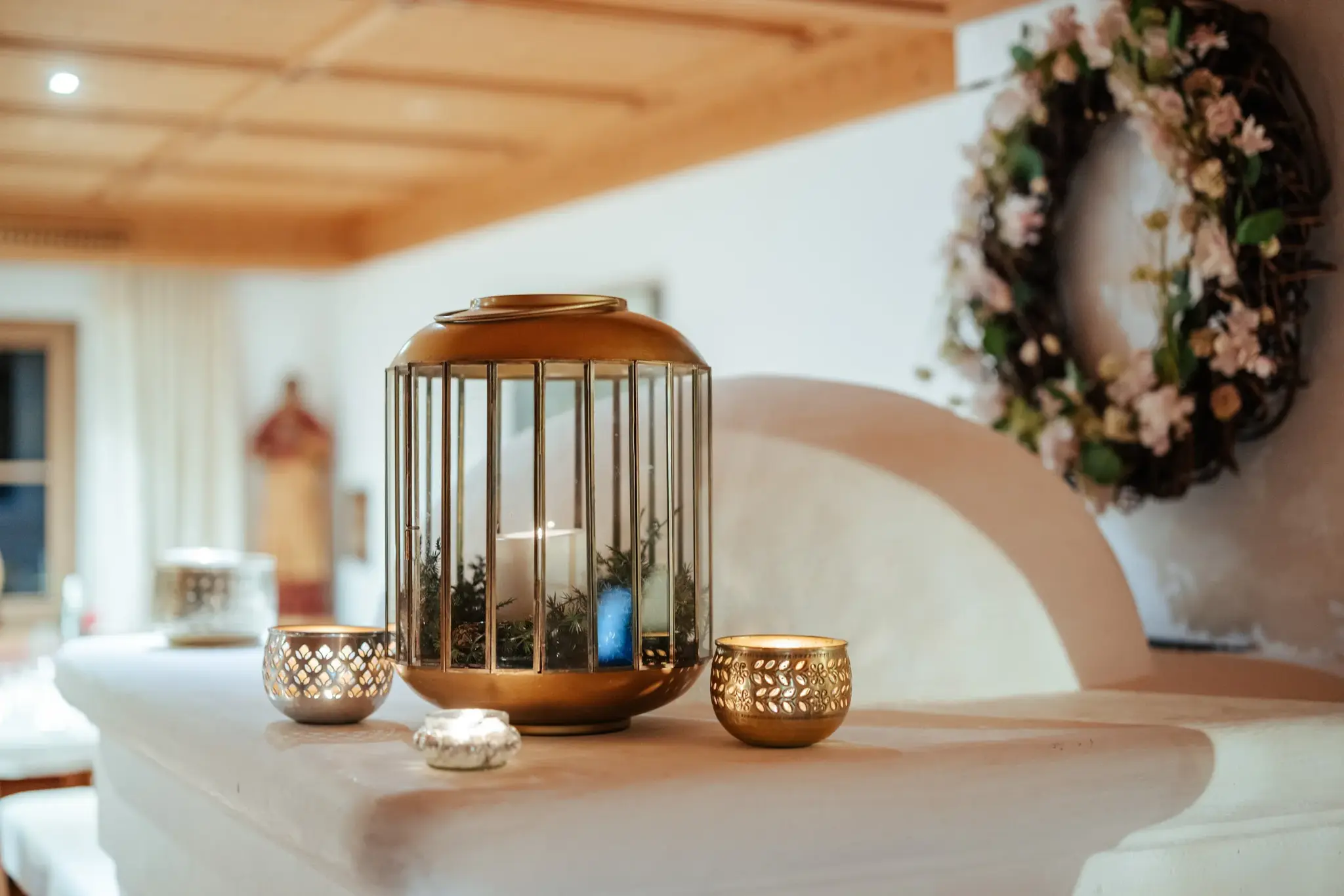Golden lantern and tea lights on the tiled stove with a wreath of blossoms, a cosy atmosphere at Biohotel Schweitzer
