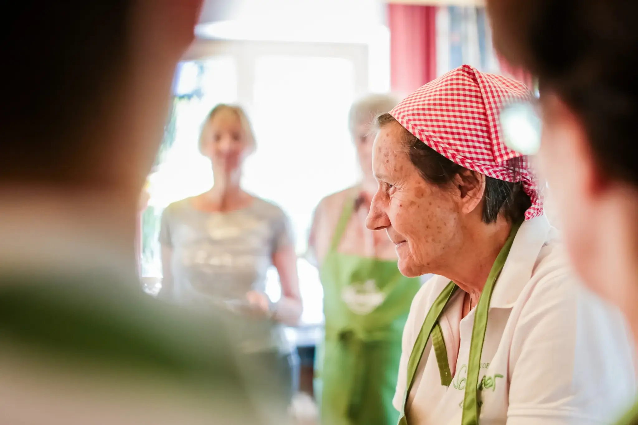 Smiling cook in a red-and-white headscarf and green apron at an organic cooking class at Biohotel Schweitzer