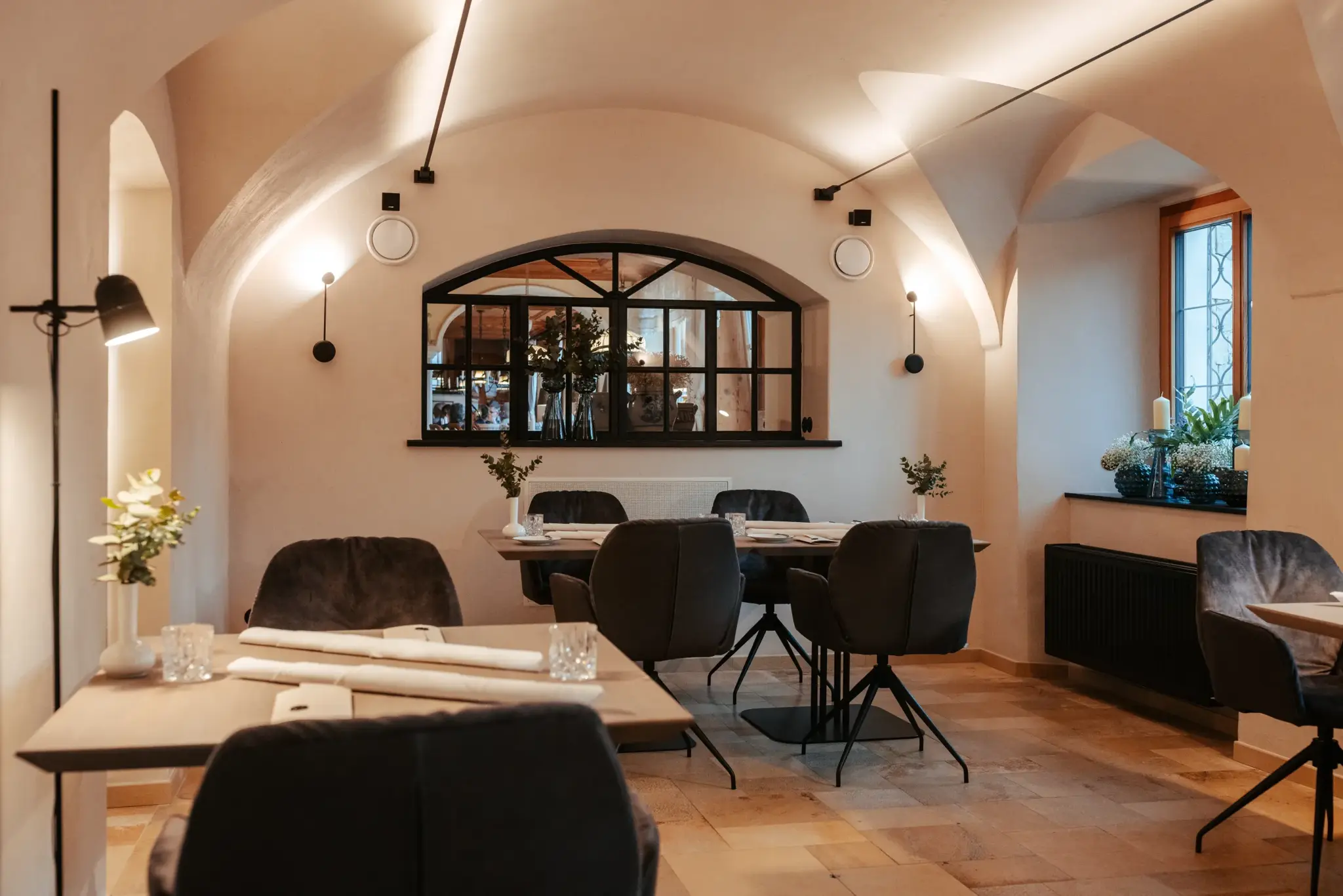 Vaulted dining room with a cream-coloured cross vault, dark velvet chairs and an arched window at Restaurant 141 in Alpenresort Schwarz