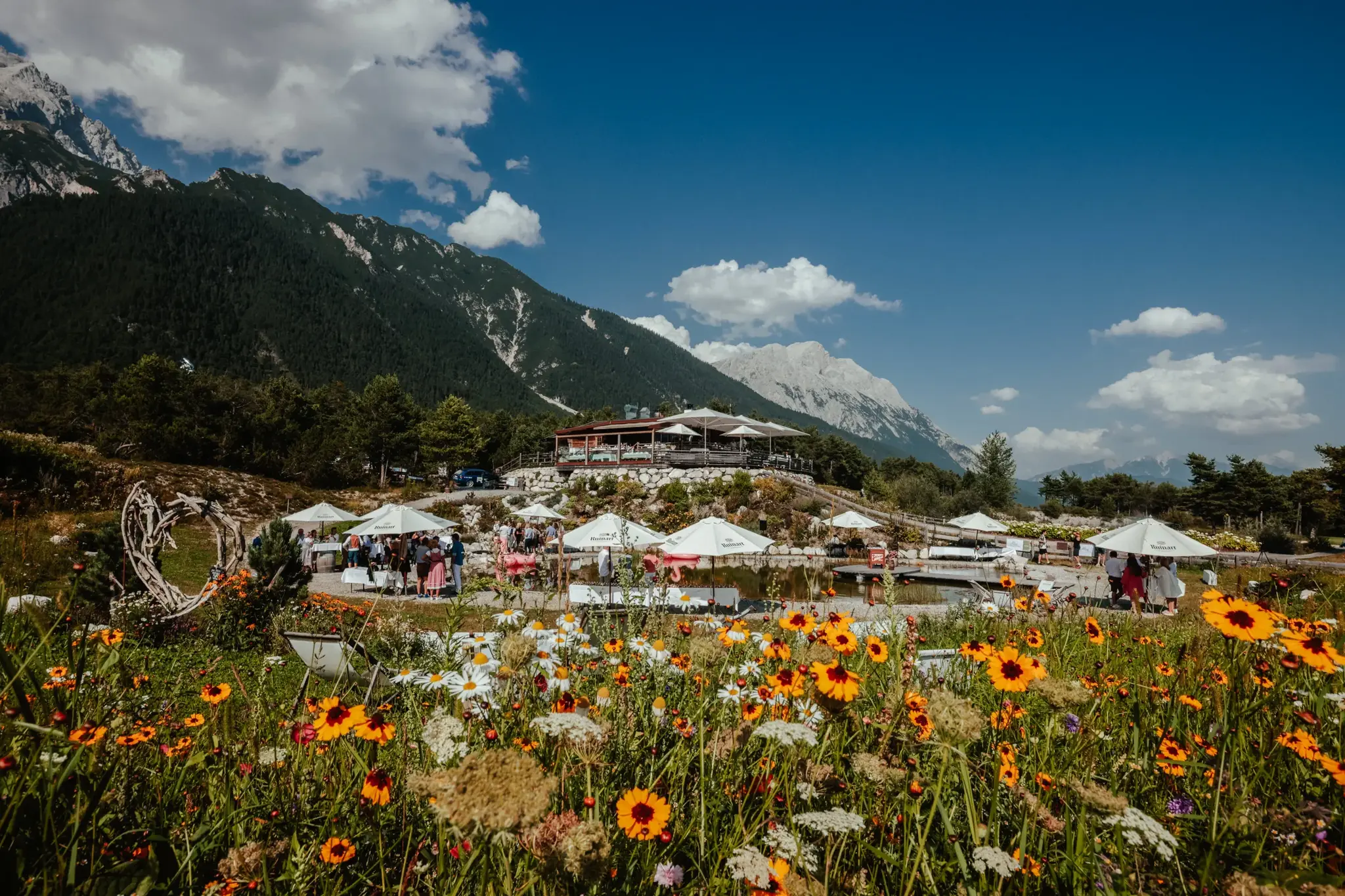 Summer party at the Stöttlalm with parasols, bathing pond and a blooming flower meadow before a mountain panorama in Tyrol