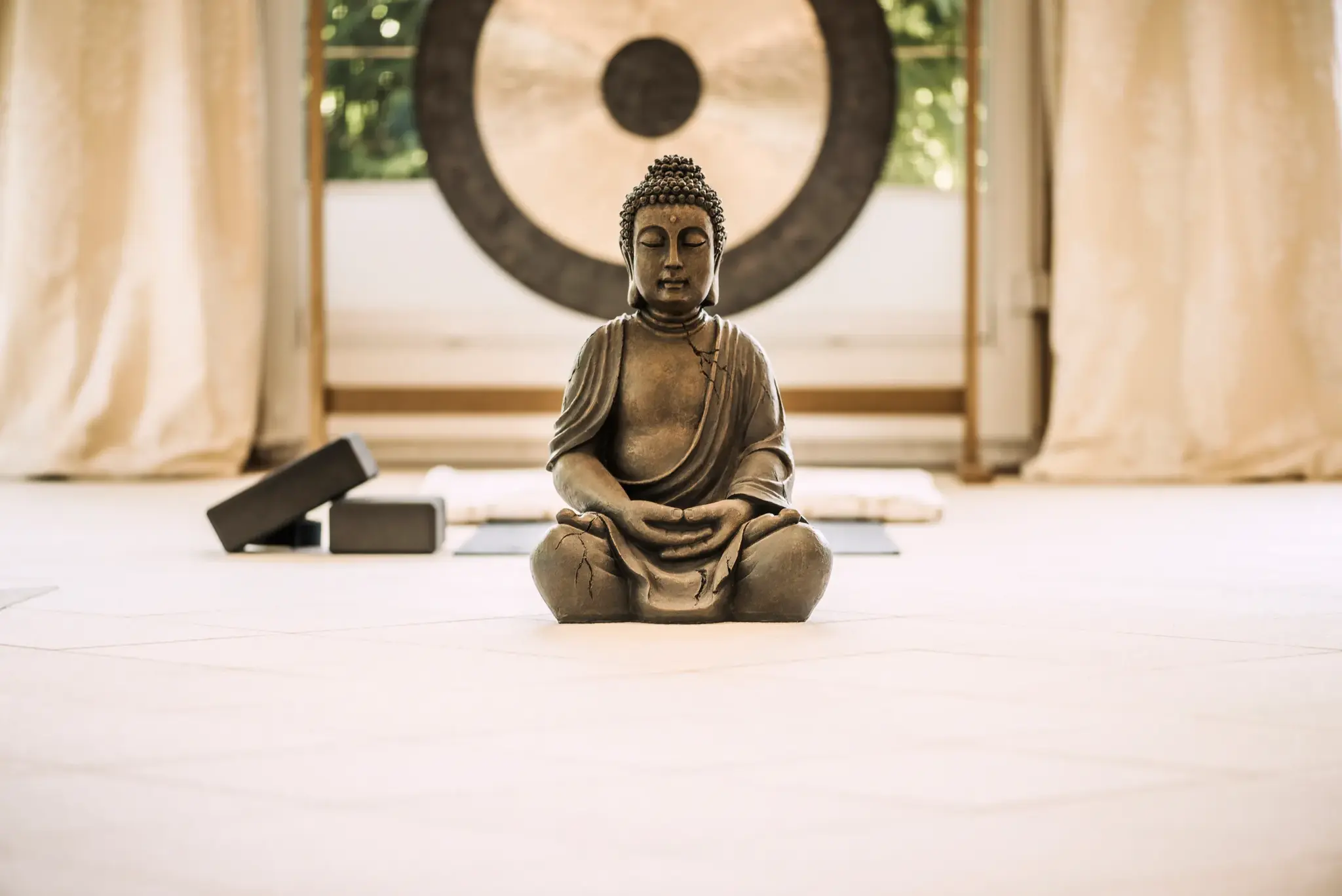 Meditierende Buddha-Statue mit Gong und Yogamatte im lichtdurchfluteten Yogaraum des Biohotel Schweitzer in Tirol