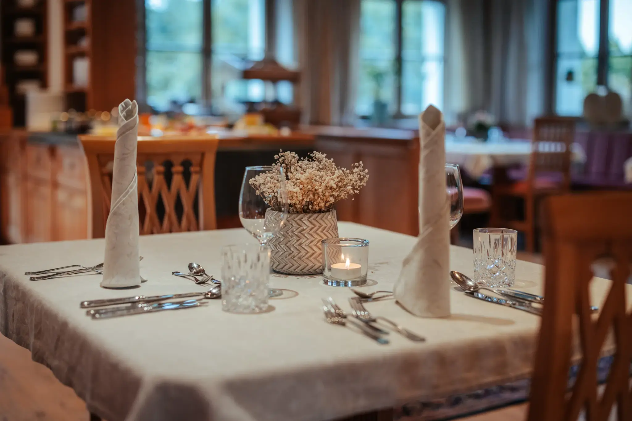 Festlich gedeckter Tisch mit gerollten Leinenservietten, Kristallgläsern und Kerzenlicht im Restaurant Greenvieh
