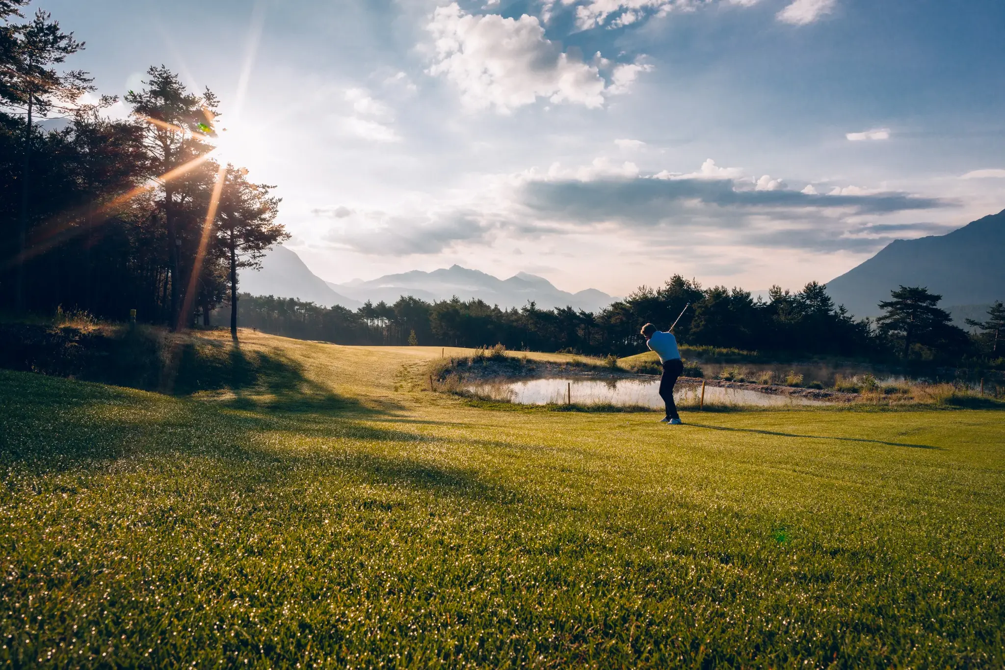 Golfer beim Abschlag im goldenen Abendlicht auf dem Golfplatz am Mieminger Plateau mit Bergen und Teich in Tirol