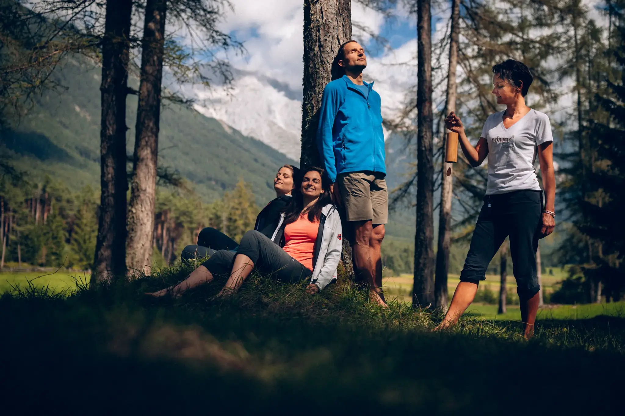 Group relaxing during forest bathing with a sound chime by a larch tree before the Tyrolean mountains