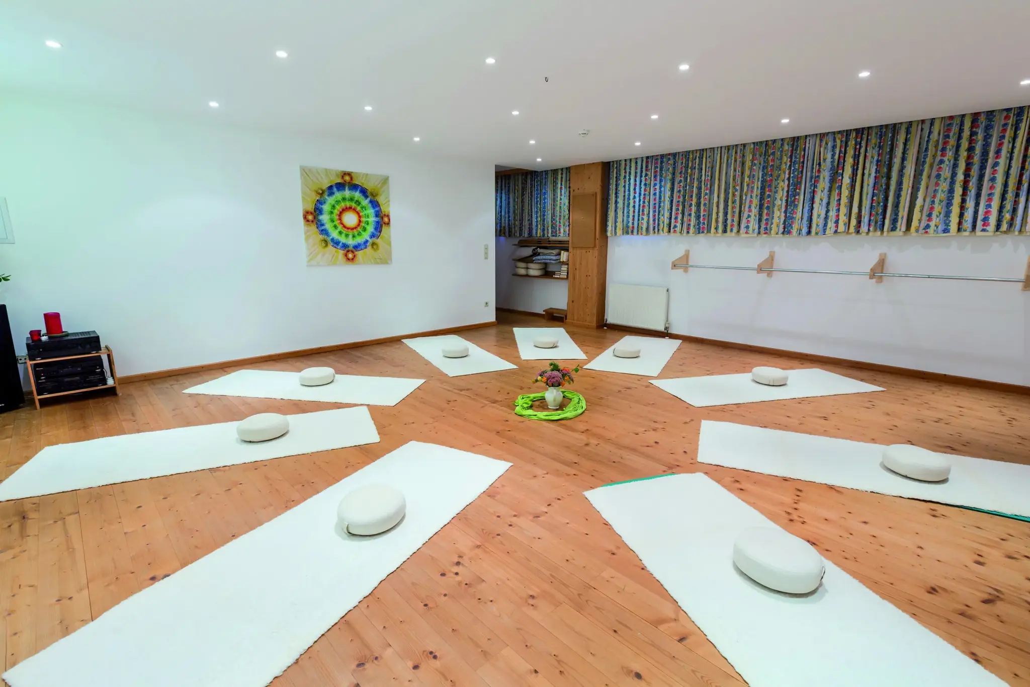 Heller Yoga- und Meditationsraum mit sternförmig ausgelegten Matten, Sitzkissen und Mandala im Biohotel Schweitzer